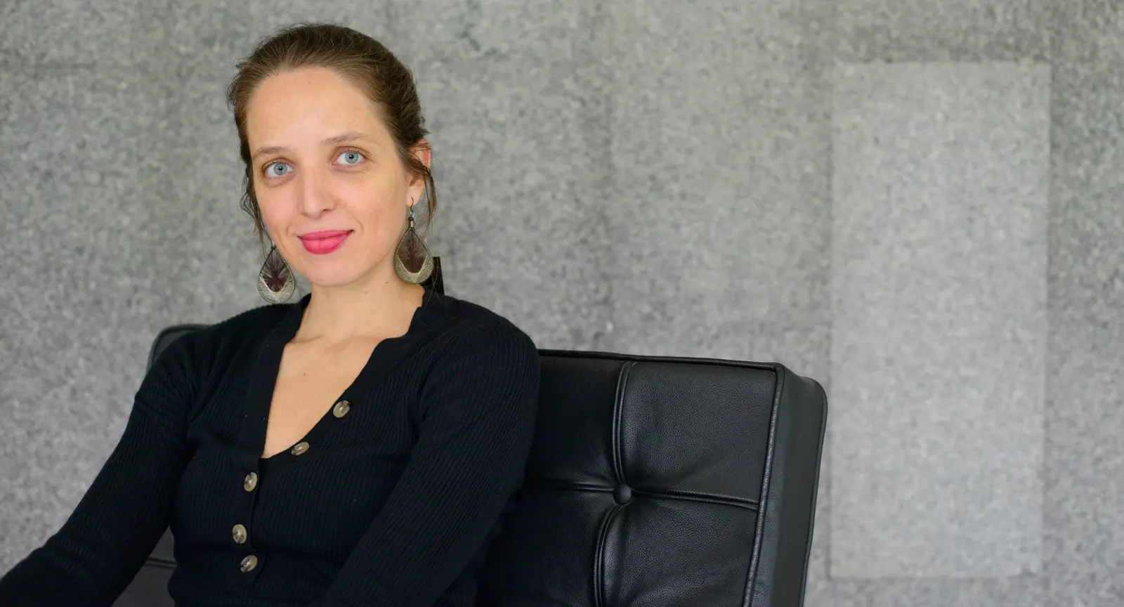 Mirella Duarte sentada em uma poltrona, diante de uma parede de granito
